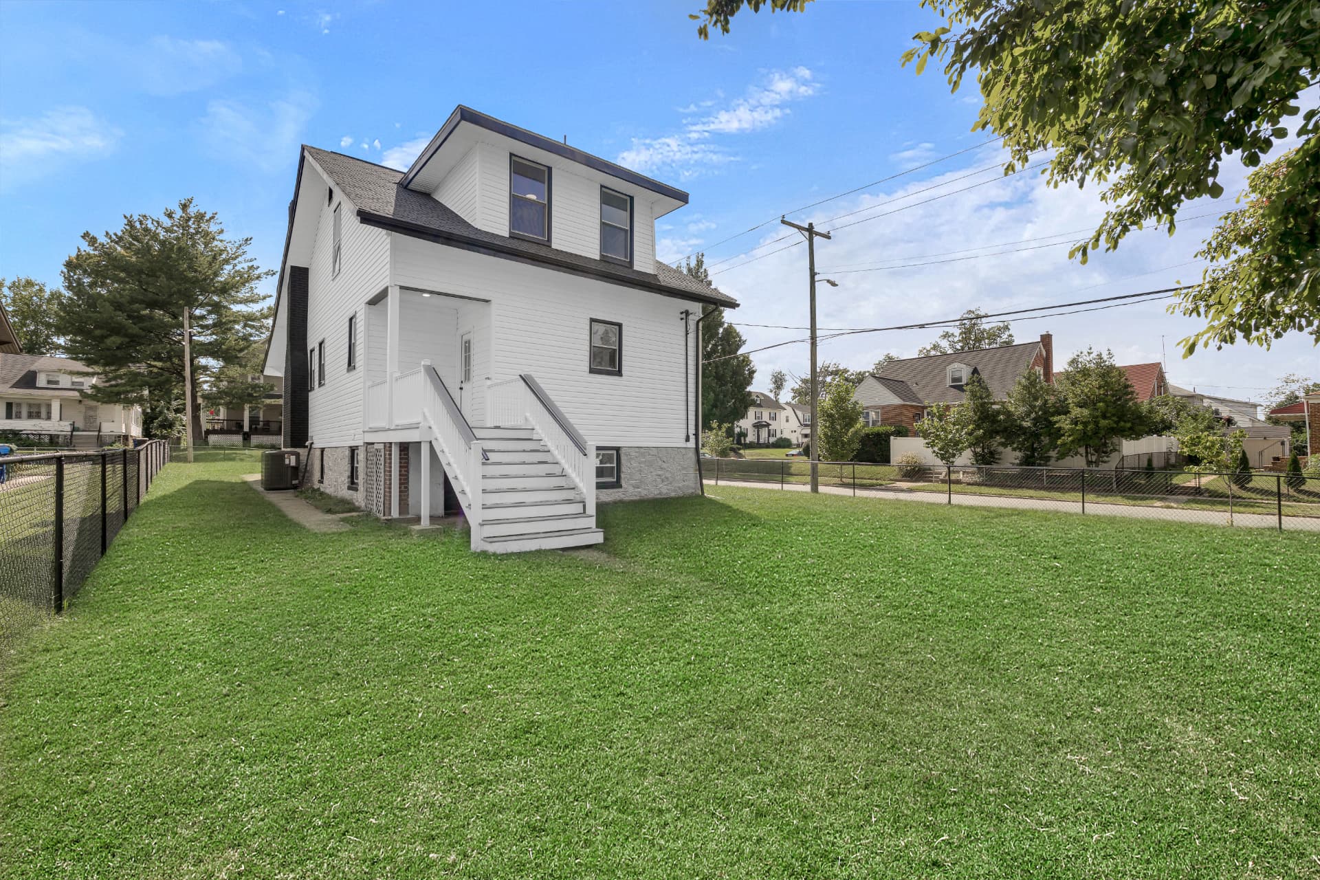 Side yard view of a renovated white home with fenced green lawn and rear deck stairs