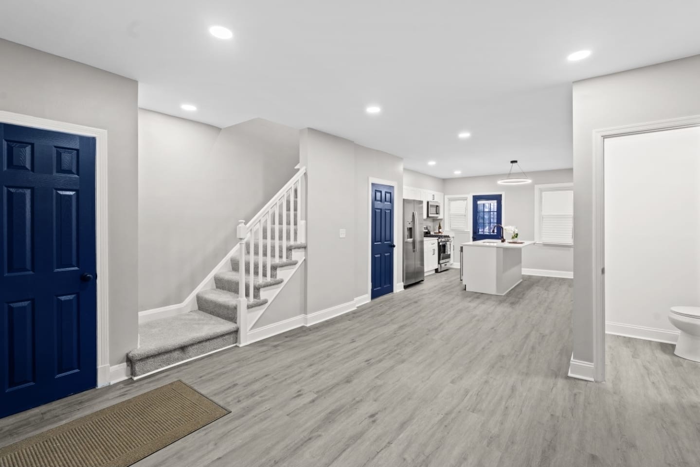 Open entry and kitchen with navy doors and light wood flooring