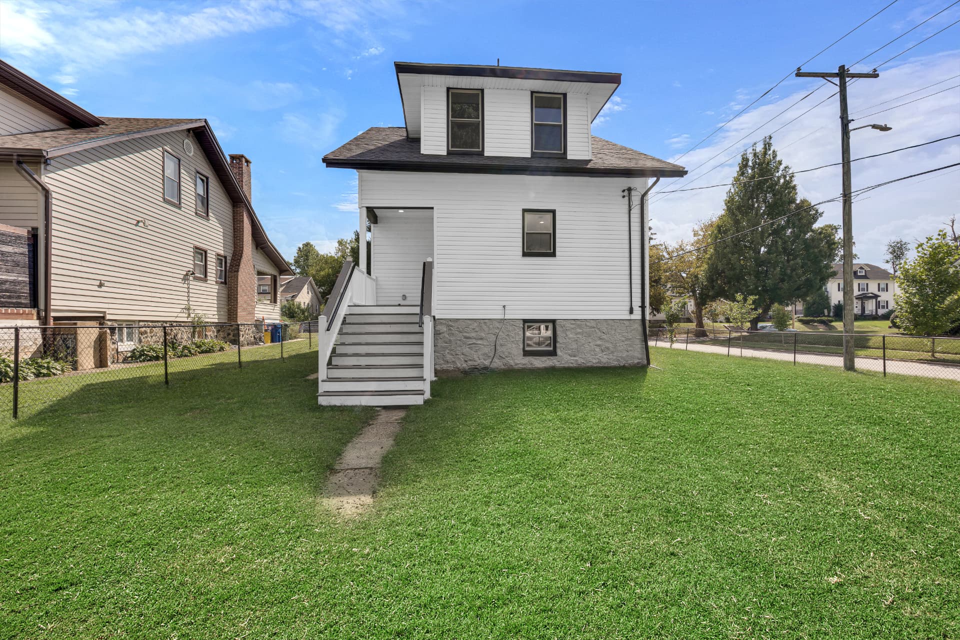 Rear exterior of a renovated white two-story home with stone foundation and rear stair entry
