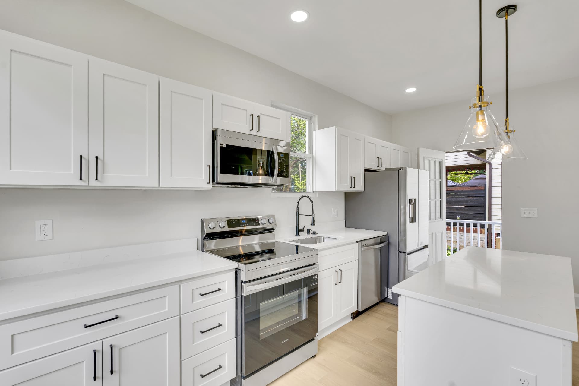 Renovated white shaker kitchen with quartz counters, stainless appliances and glass pendant lights