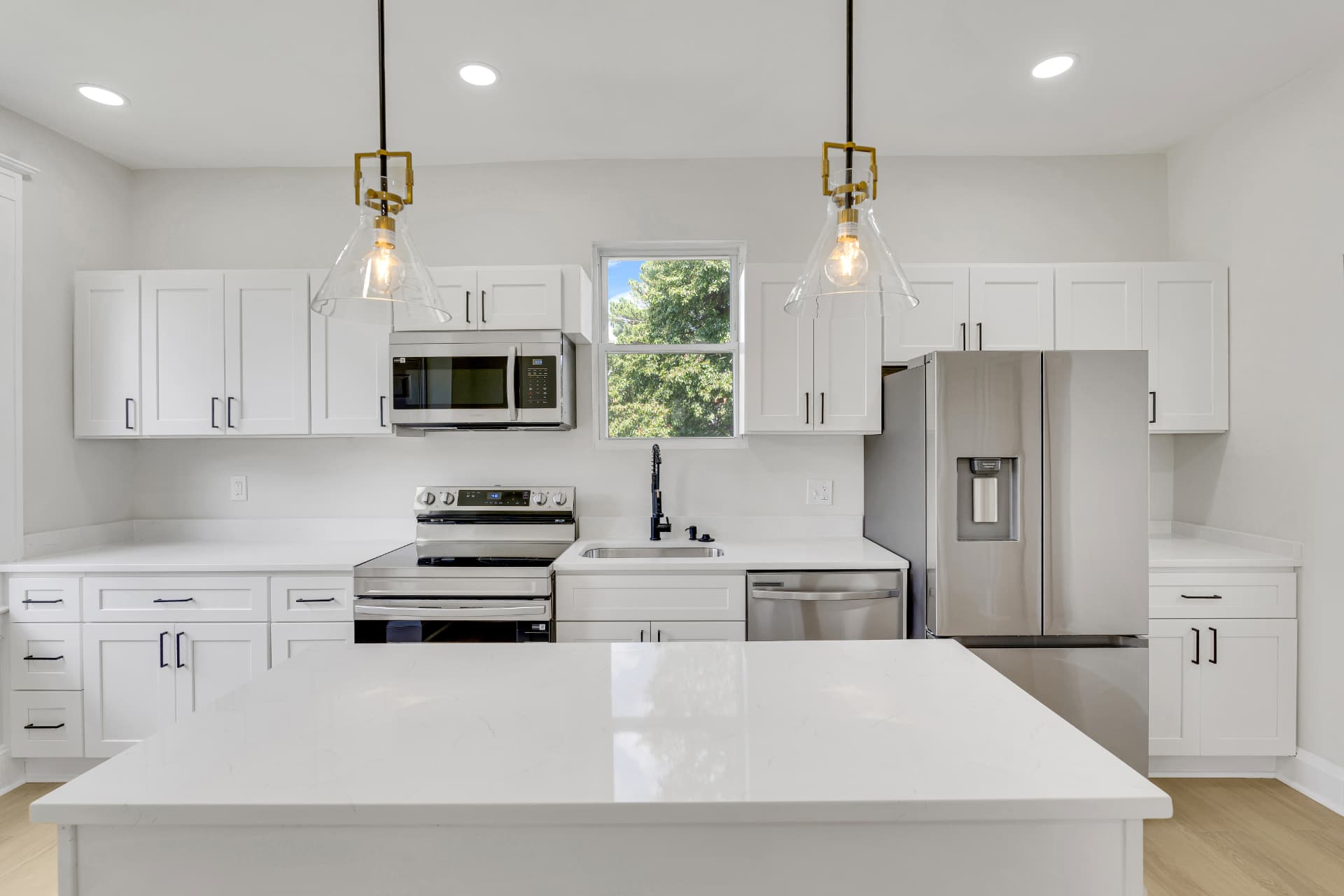 Wide view of a white kitchen with a large quartz island and twin glass pendant lights