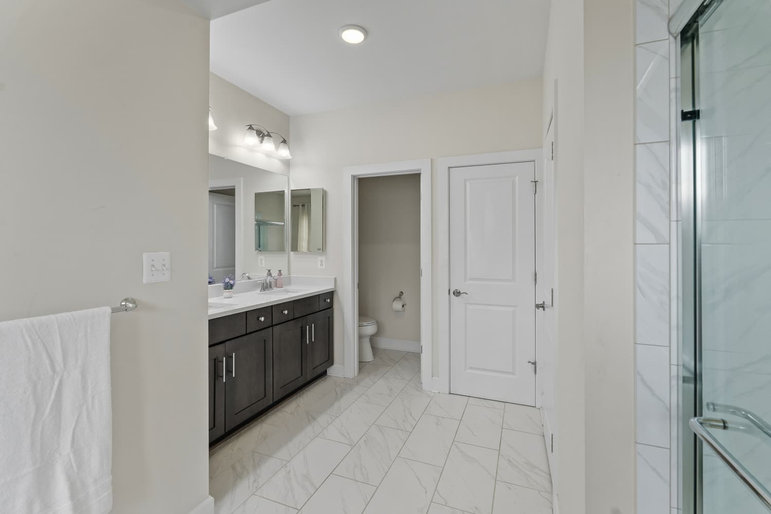 Primary bathroom with dark wood double vanity, marble tile and glass shower