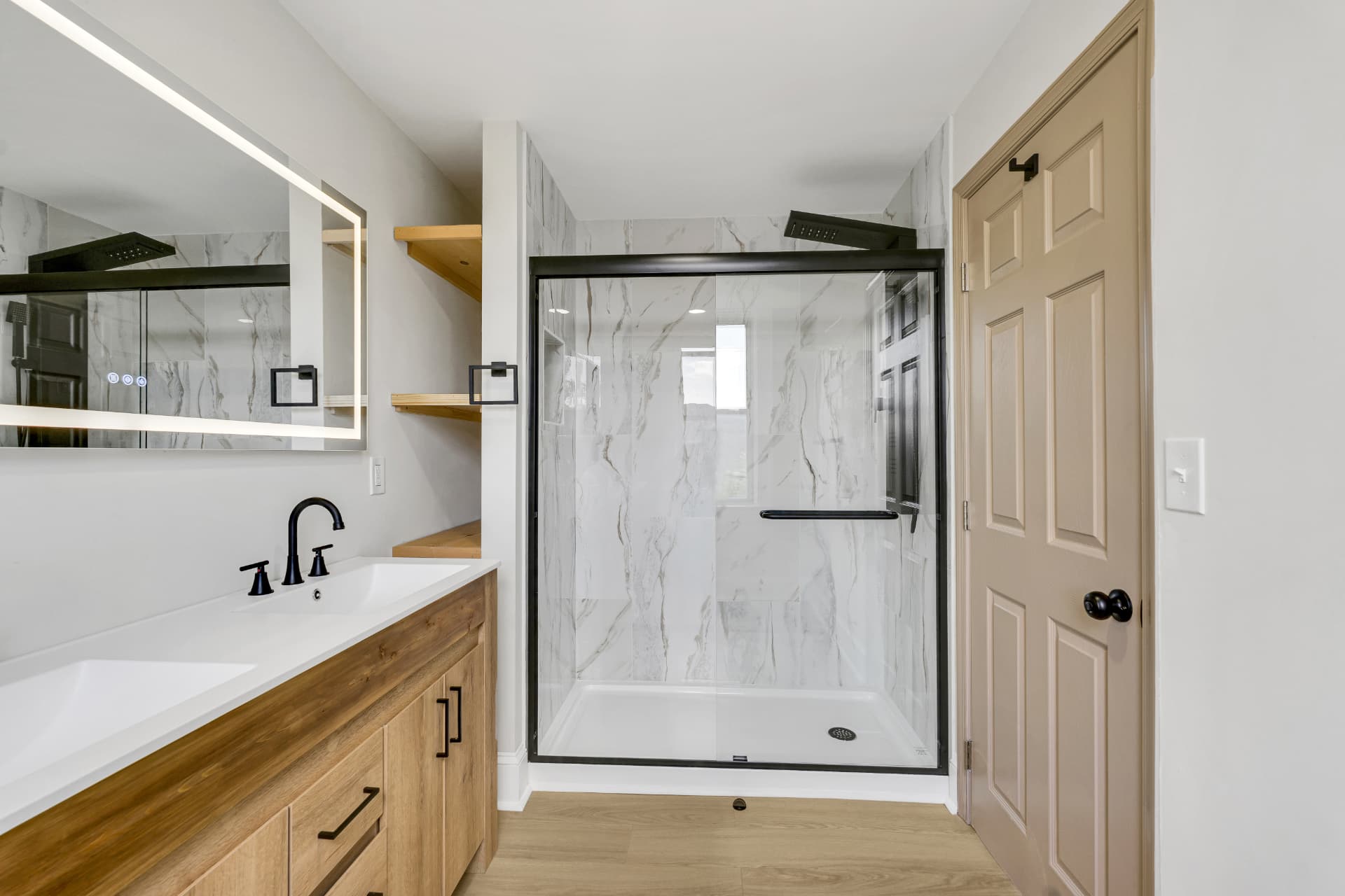 Primary bathroom with double wood vanity, backlit mirror and marble-tiled glass shower