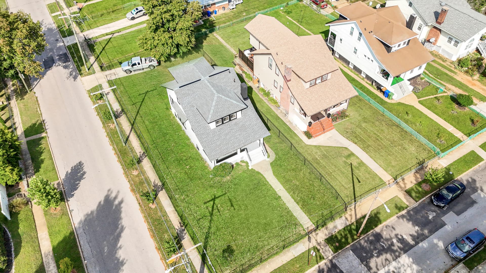 Aerial drone photo of a renovated white two-story home on a fenced corner lot