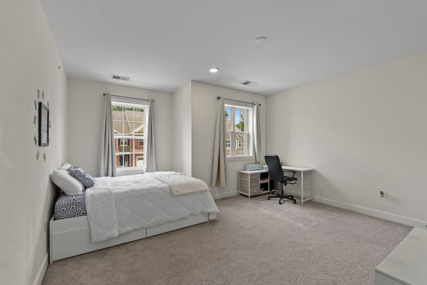 Bright carpeted bedroom with two windows and a desk